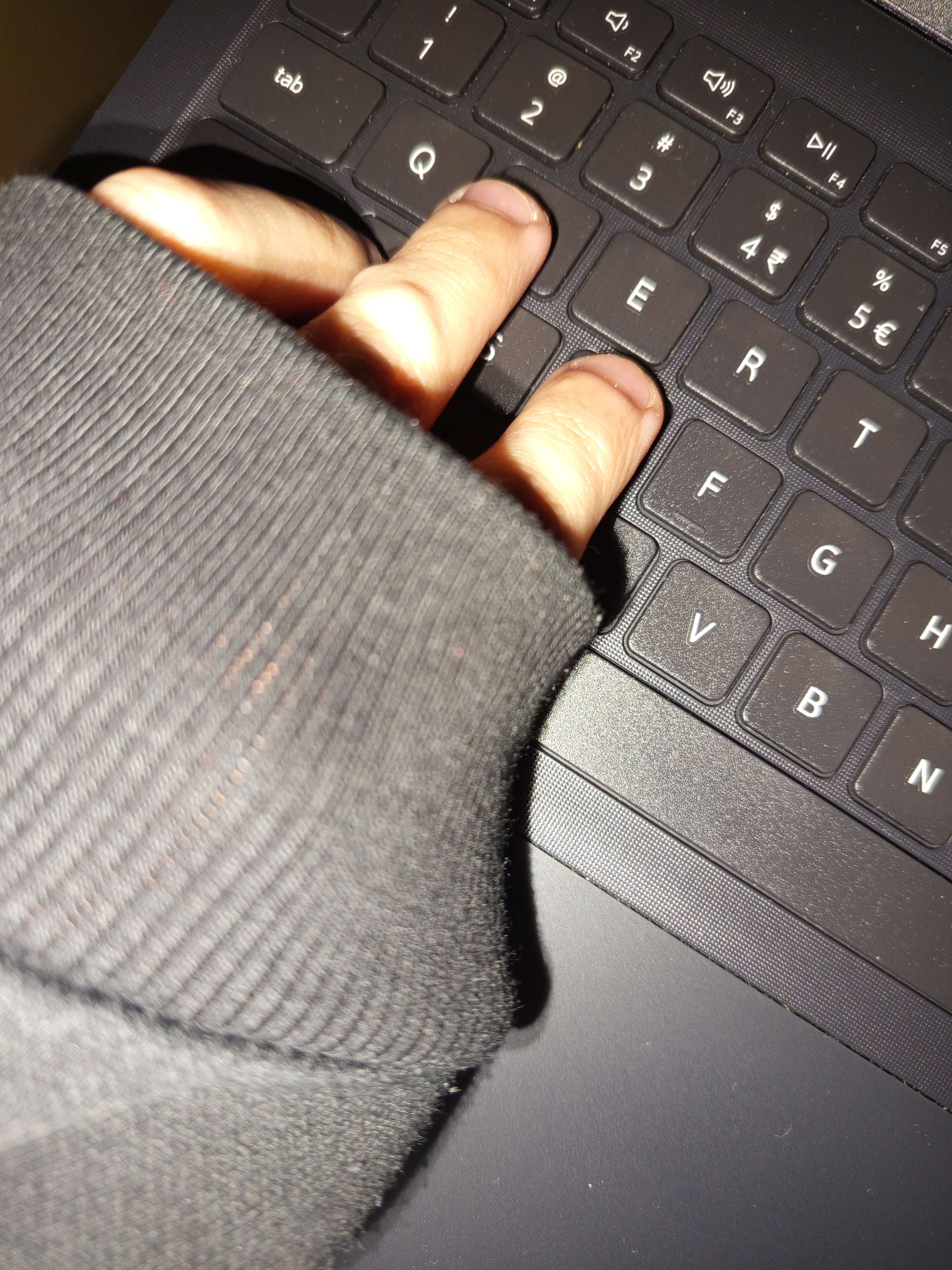 Hand with hoodie sleeve pulled over fingers, resting on a laptop.